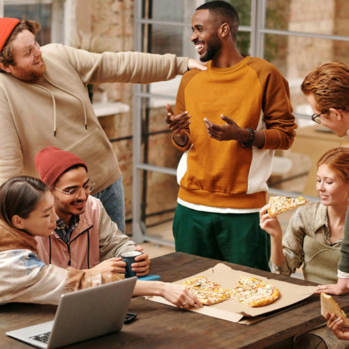 A group of business people sat around a table laughing and eating pizza