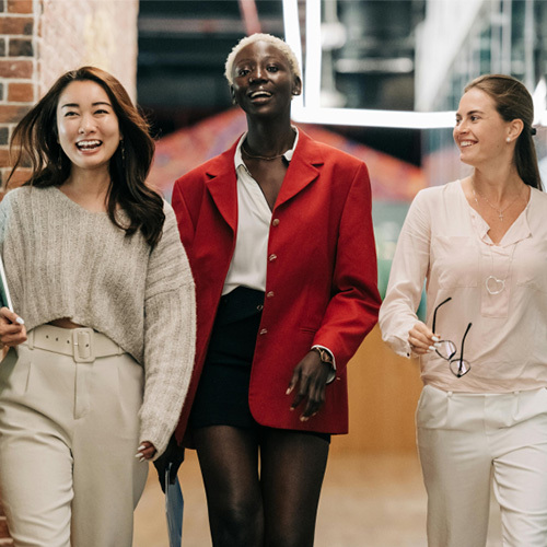 Three business woman of Asian, African American, and Caucasian descent smiling and walking down a corridor