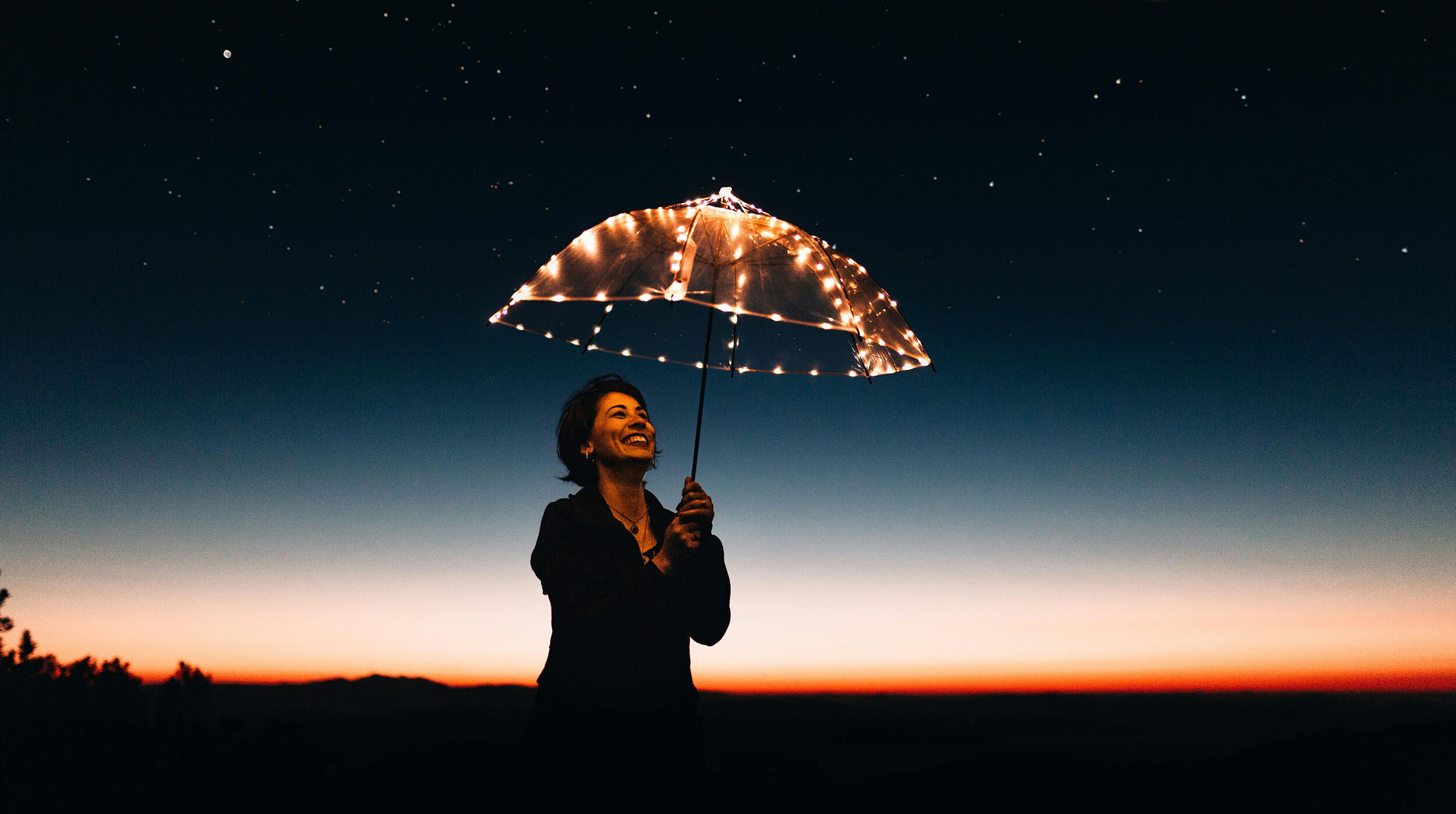 A woman looking up at the night sky through a transparent umbrella